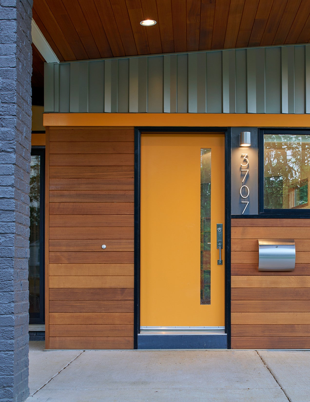 A modern home entrance featuring a bright yellow front door, wooden paneling, and sleek metallic accents with the address "3707" displayed.